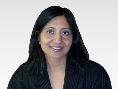 Photograph of Miss Sangeeta. She has a smiling face with her flowing hair left over her black coat with stripes