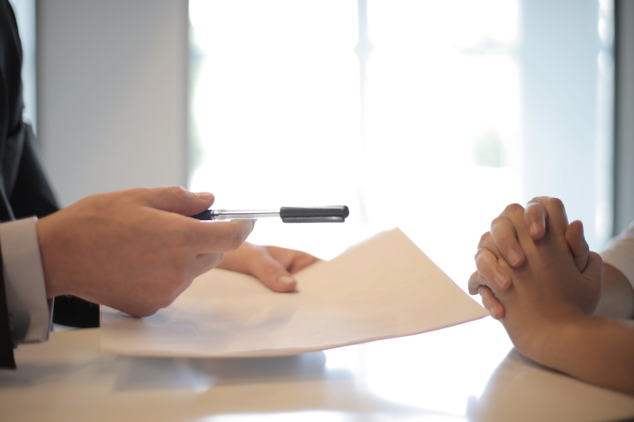 A picture showing the hand a boss holding a sheet of paper and pen handing over to his client for signing of a deal whose hands are interlocked in deciding to sign.